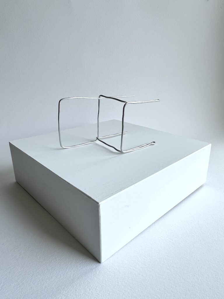 Small aluminium wire chair lying on its side on a white panel, angled view